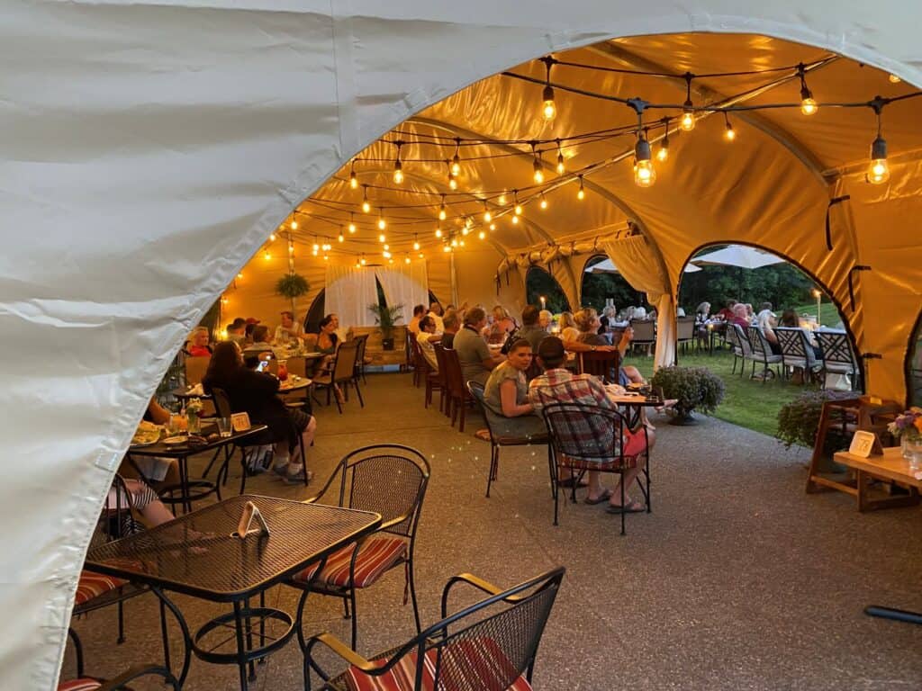 Outdoor wedding reception under a large tent with string lights and guests dining.