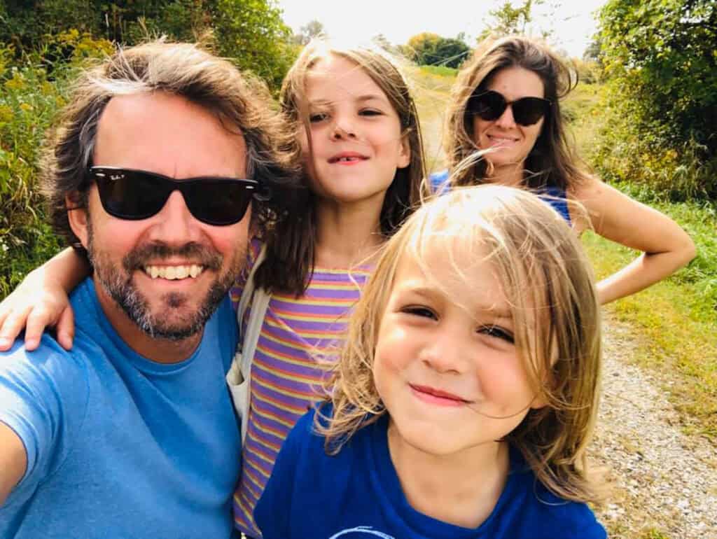 Family of four on a sunny outdoor walk in Vermont with trees and greenery.