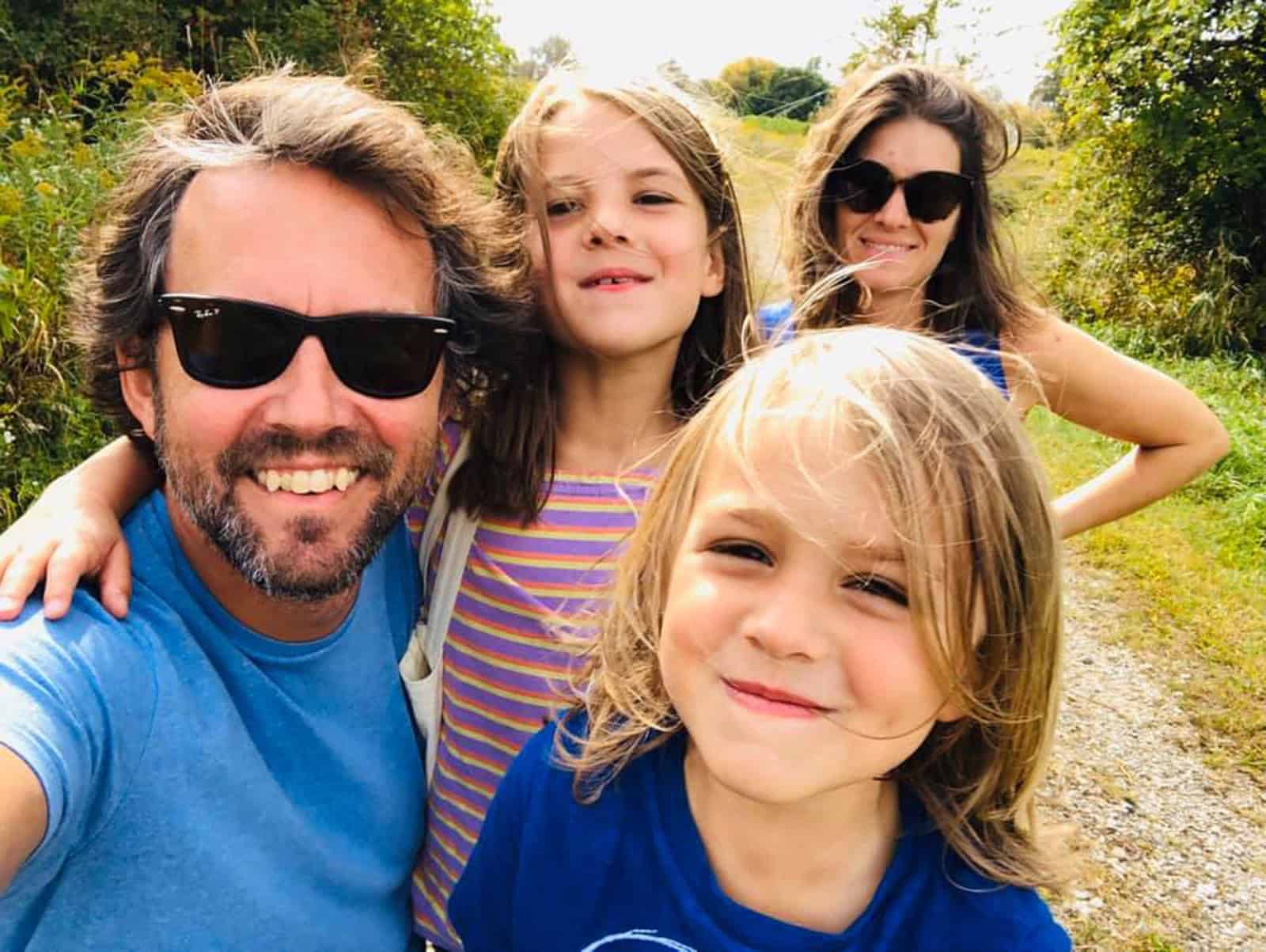 Family of four on a sunny outdoor walk in Vermont with trees and greenery.