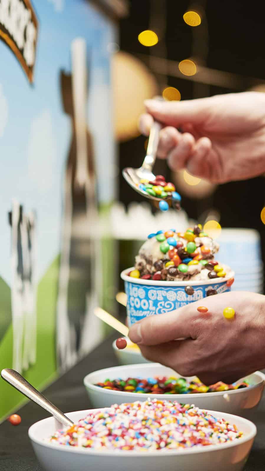 Person adding colorful toppings to ice cream at Vermont wedding event.