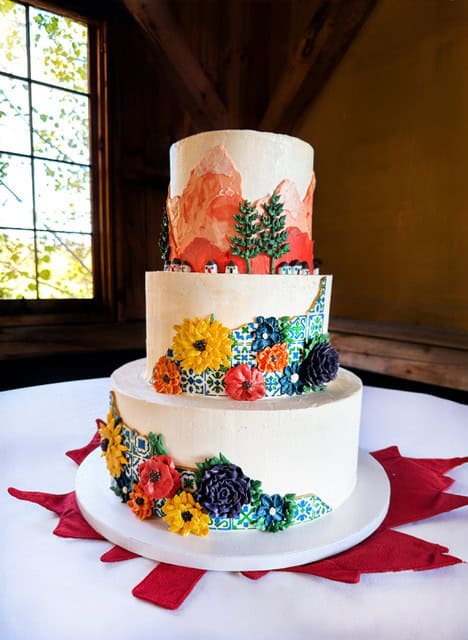 Elegant three-tier wedding cake with colorful floral and nature-themed decorations.