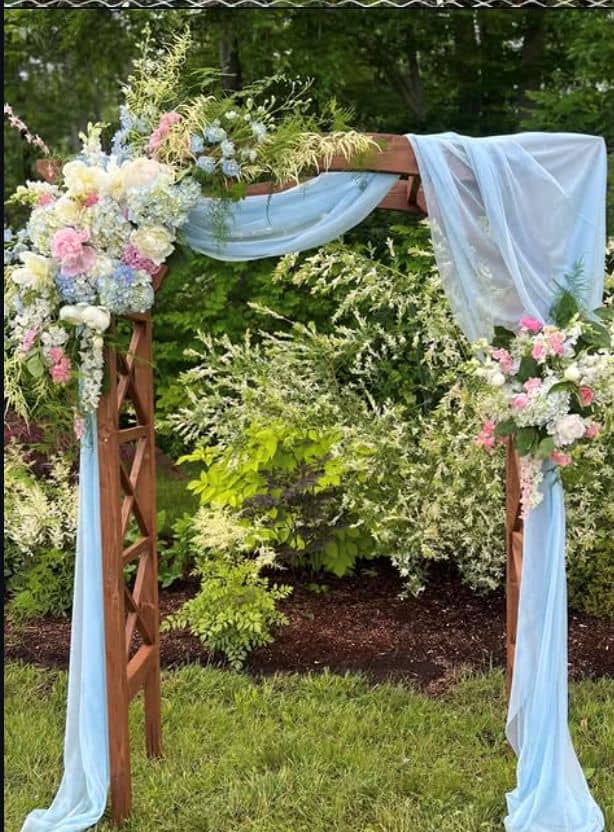 Beautiful wedding arch decorated with pastel flowers and light blue fabric in a garden setting.