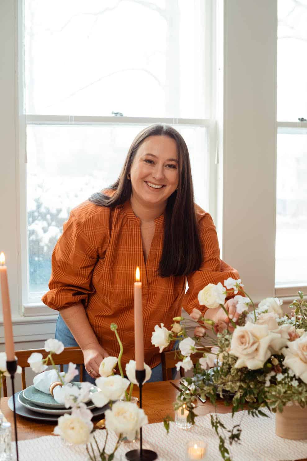 Smiling woman at wedding table with floral arrangements and candles.