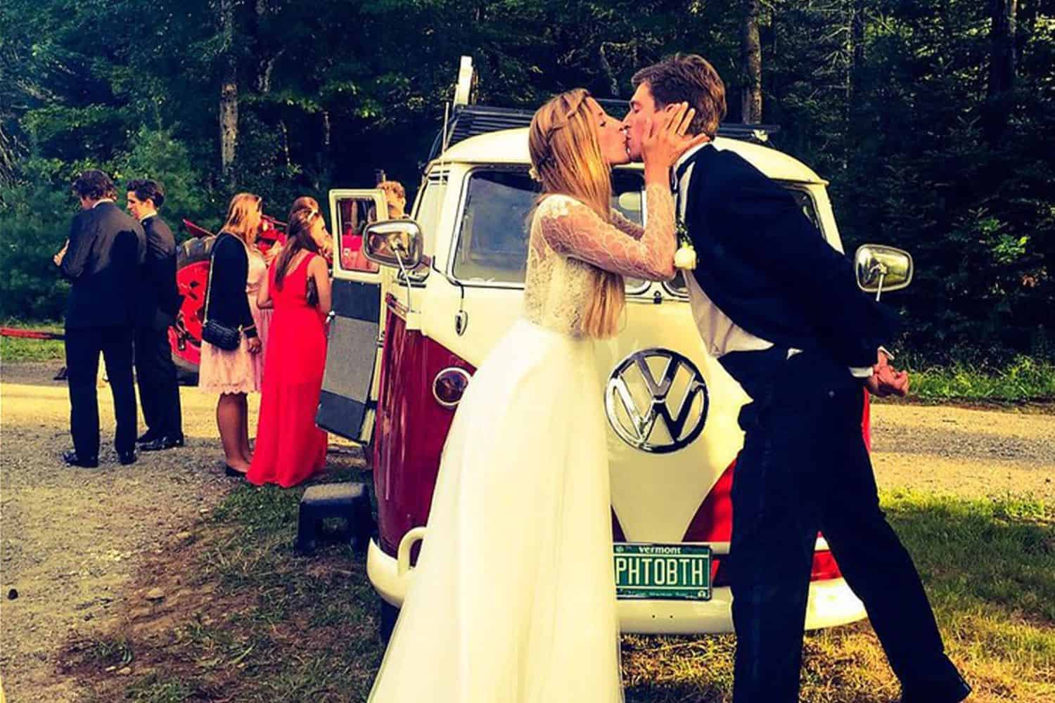 Bride and groom kissing in front of vintage Volkswagen van at wedding.