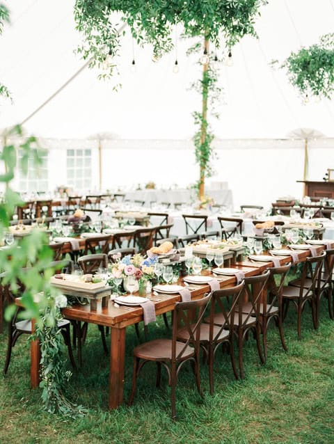 Elegant outdoor wedding reception with long wooden tables and floral centerpieces.