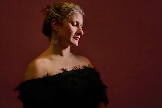 Elegant woman in black dress with earrings, profile view, dark red background.