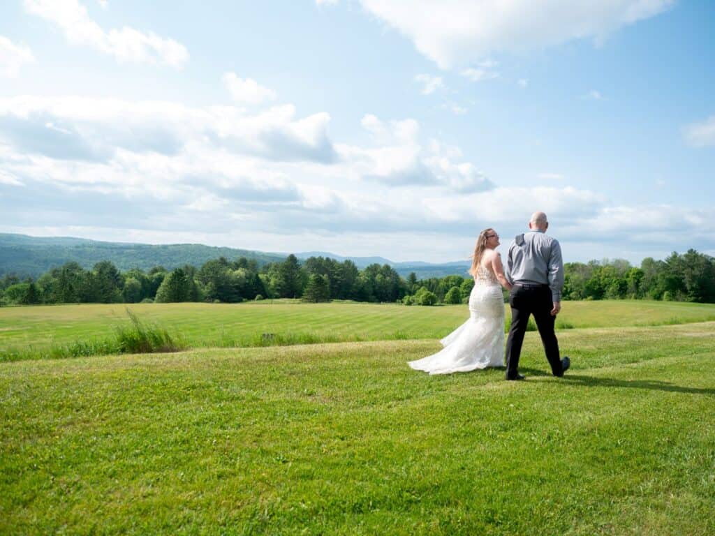 Bride and groom standing on a lush green field with scenic mountains in the background.